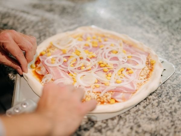 Pizza wird frisch belegt Frisch belegte Pizza mit ausgewählten Zutaten in der Küche von Giuseppe